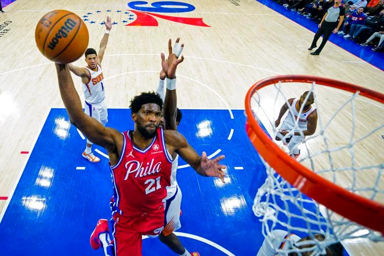 Joel Embiid, in red jersey No.21, soars for a dunk in a match against the Phoenix Suns. The Sixers lock up Embiid for three years and USD192.9 million contract extension.