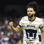 Cesar Huerta, in striped white DHL shirt, pumps his fist during a match. Huerta shared a failed move to transfer from Pumas to Liverpool