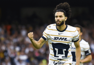 Cesar Huerta, in striped white DHL shirt, pumps his fist during a match. Huerta shared a failed move to transfer from Pumas to Liverpool