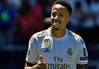 Eder Militao, in white uniform, flashes a sign of approval during a match.