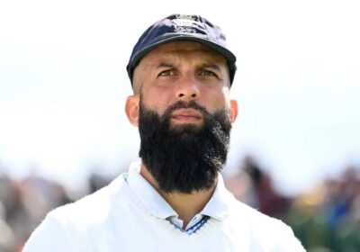 Moeen Ali, in white uniform, looks on during a break from a match. Ali recently announced his retirement from international cricket