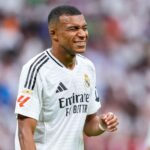 Kylian Mbappe, in an Emirates' white jersey, grins during a break in action. Mbappe awaits the outcome of a French leaue order to make PSG pay for his unpaid wages