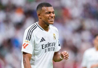 Kylian Mbappe, in an Emirates' white jersey, grins during a break in action. Mbappe awaits the outcome of a French leaue order to make PSG pay for his unpaid wages