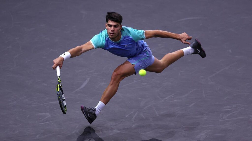 Carlos Alcaraz of Spain, in blue shirt and shorts, rushes to return the serve at the 2024 Rolex Paris Masters on Tuesday. Alcaraz advances in Paris Masters;