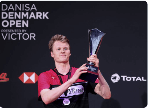 Anders Antonsen, in red and black shirt, holds the trophy after winning the men's singles final. Andersen, Wang win 2024 Denmark Open