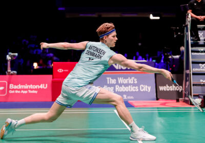 Anders Antonsen, in white-gray uniform, returns a shot in the men's singles final in Odense. Andersen, Wang win 2024 Denmark Open.