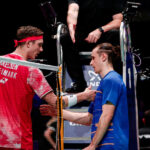 Viktor Axelsen, in red unoiform, shakes hand of Frenchman Alex Lanier after their match. Axelsen forced to quit at Denmark Open due to sickness.