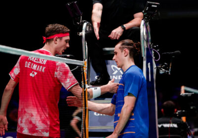 Viktor Axelsen, in red unoiform, shakes hand of Frenchman Alex Lanier after their match. Axelsen forced to quit at Denmark Open due to sickness.