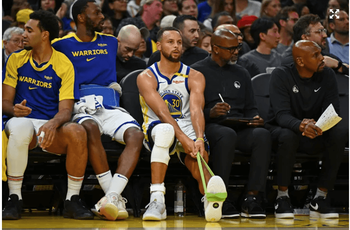 Golden State guard Stephen Curry, center, in white jersey, sits on the bench to rest his left ankle in his team's match against the Los Angeles Clippers on Sunday. Curry twists ankle as Warriors lose