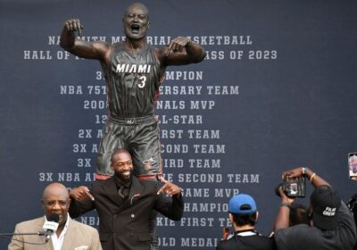 Retired Miami Heat legend Dwyane Wade, in black suit, mimics the pose of his new statue outside the Heat's team arena on Sunday. Wade explains new statue look, cites 'artistic version' of a moment