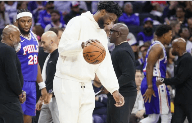 Philadelphia center Joel Embiid, in white sweater and pants, playfully dribbles the ball as the Sixers prepare against the Detroit Pistons on Wednesday. Sixers fined for misleading Embiid injury statements