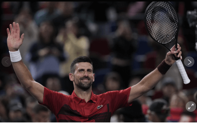 Novak Djokovic, in red shirt and shorts, acknowledges the crowd in Shanghai. Djjokovic advances to the Shanghai Open fourth round