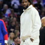 Philadelphia center Joel Embiidm in white sweater and pants, looks on as the Sixers prepare against the Detroit Pistons on Wednesday. Sixers fined for misleading Embiid injury statements