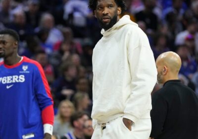 Philadelphia center Joel Embiidm in white sweater and pants, looks on as the Sixers prepare against the Detroit Pistons on Wednesday. Sixers fined for misleading Embiid injury statements