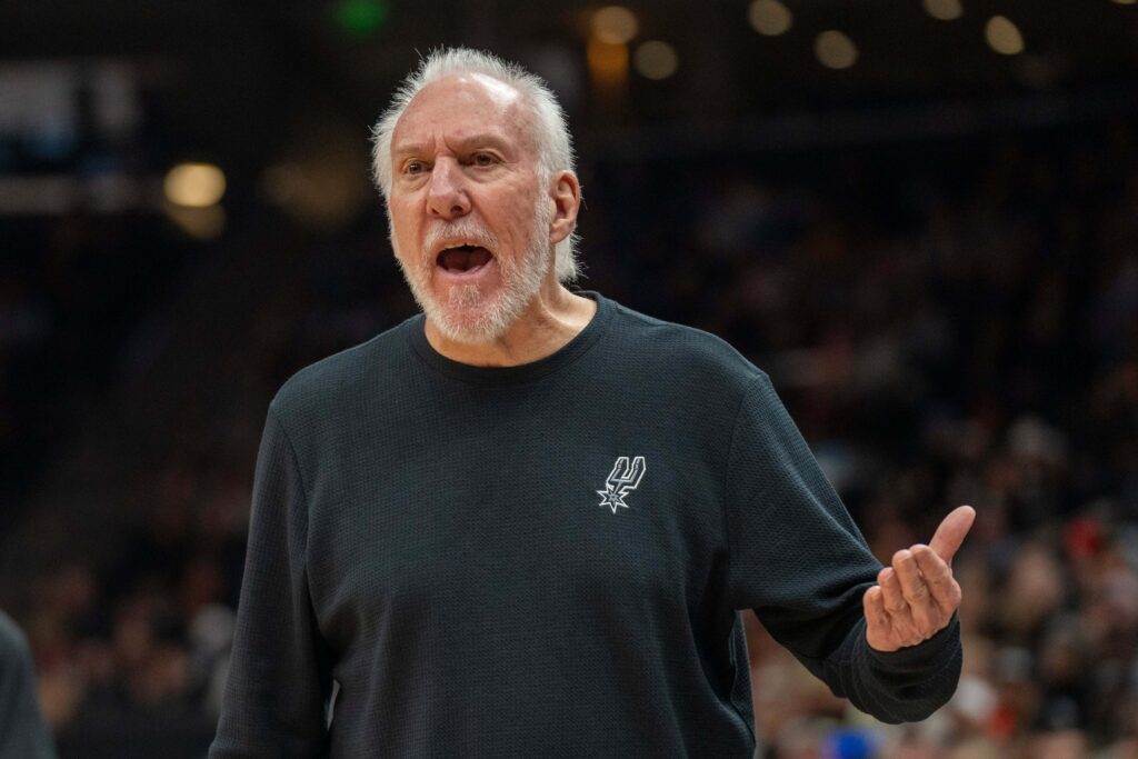 Coach Gregg Popovich, in black ssweater, hollers instructions from the sideline at an NBA game. Popovich recovering from mild stroke, says Spurs 